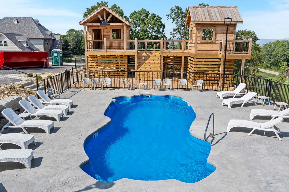 A playful exterior view of the swimming pool area, featuring wooden playhouses, lounge chairs, and ample space for children and adults to enjoy. The relaxed vibe is complemented by the playful design, inviting both families and groups to gather for sunbathing, swimming, and laughter-filled afternoons.