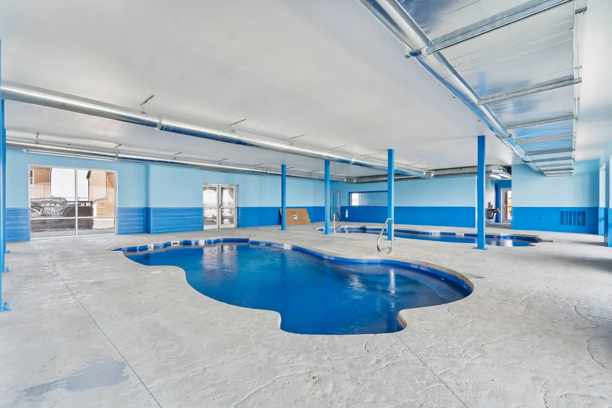 This interior image features a spacious indoor swimming pool with bright blue walls and large windows, filling the space with energizing natural light. Swimmers can enjoy the pool year-round, regardless of the weather.