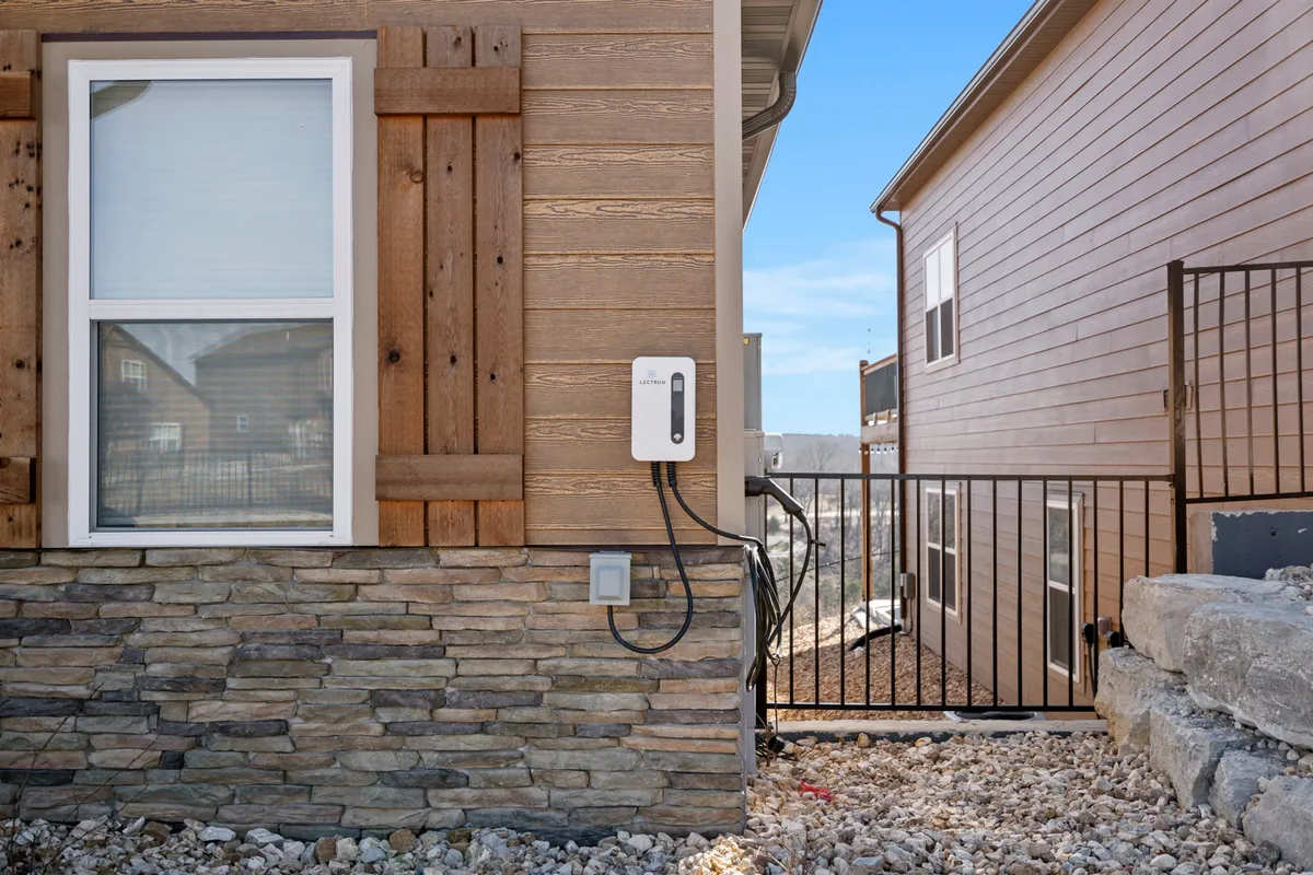 An exterior shot focusing on a window with wooden shutters, a stone façade, and a clearly visible electric vehicle charger. The scene is contemporary and welcoming, showing the resort’s commitment to eco-friendly travel options.