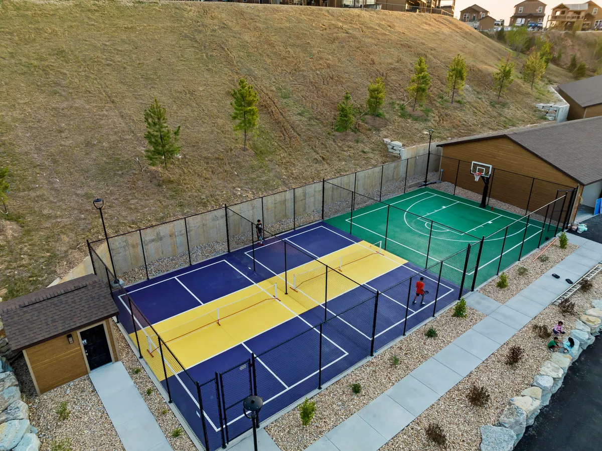 A dynamic exterior image showcasing tennis and basketball courts nestled amid lush landscaping. The courts are set up for active play, hinting at the community's vibrant recreational offerings.
