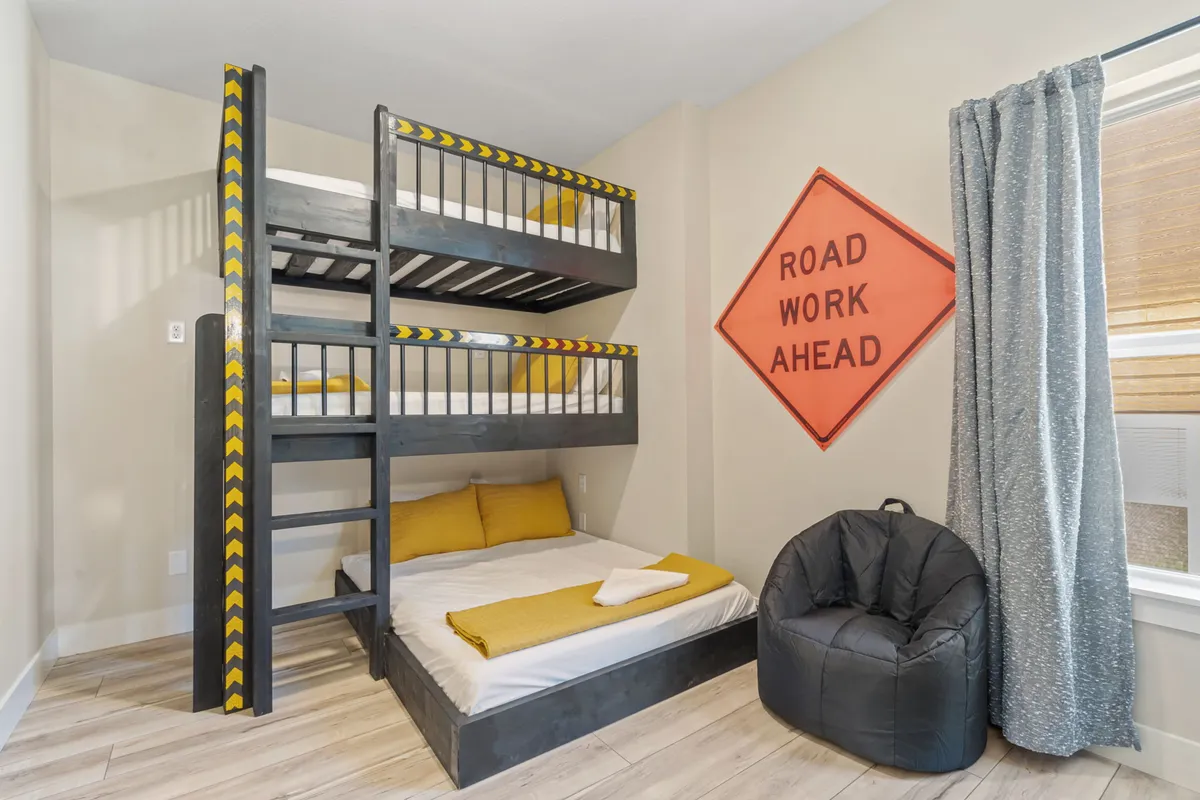 A playful bunk bedroom with two twin-over-full bunk beds, accented by a road work sign, a bean bag chair, and youthful decor. The space feels inviting and fun, perfect for children or the young at heart.