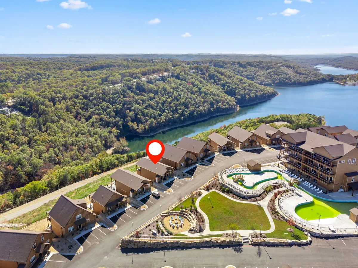 An exterior shot capturing a river, swimming pool, buildings, and surrounding greenery, creating a sense of recreational space and access to both water and nature. The scene is tranquil and recreational, evoking lakeside leisure and group enjoyment.