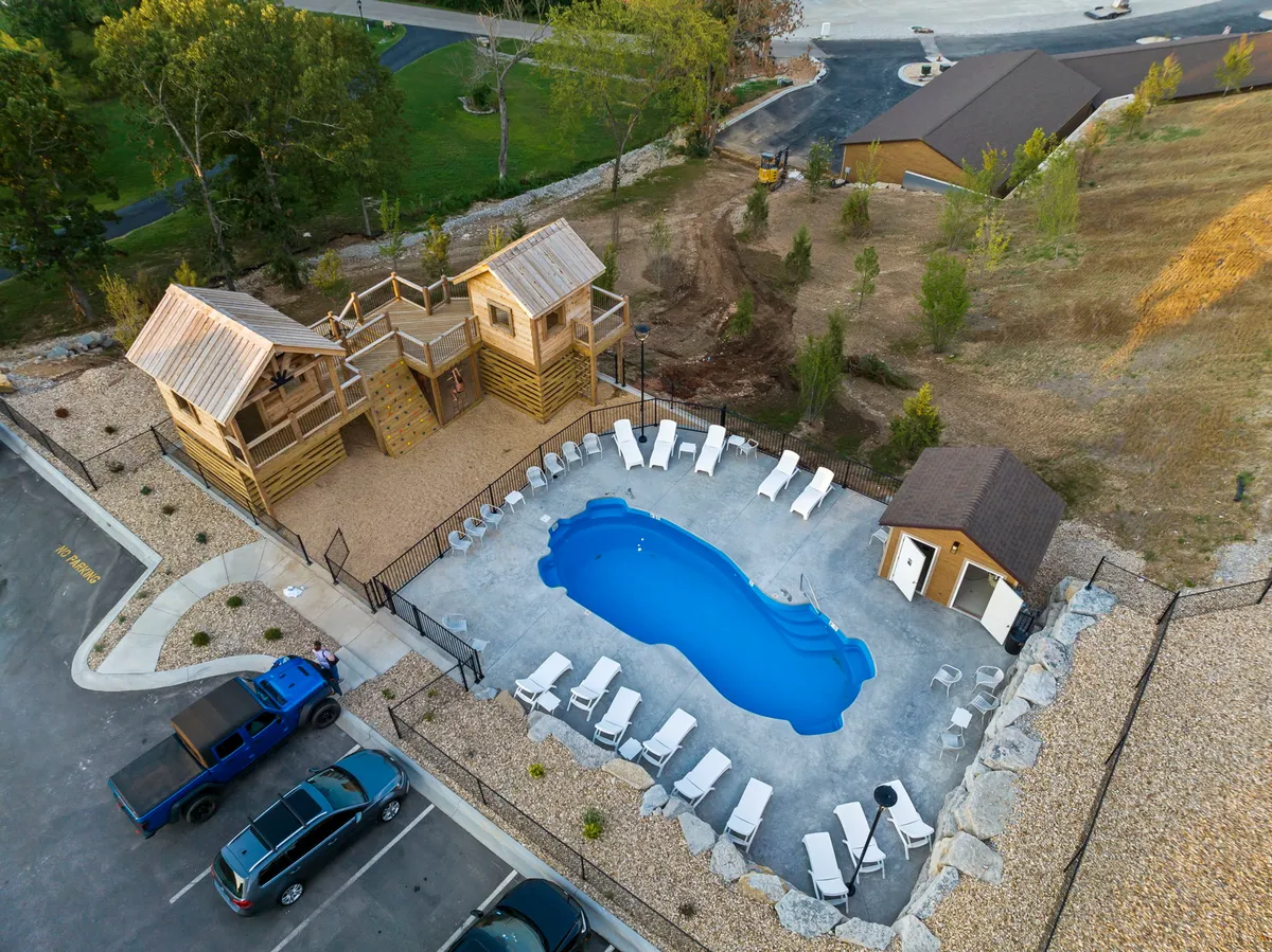 An inviting exterior scene highlighting a swimming pool, play structure, and lounge chairs set against a scenic landscape. Families are seen swimming, sunbathing, and children enjoying the play area, evoking relaxation and shared outdoor experiences.