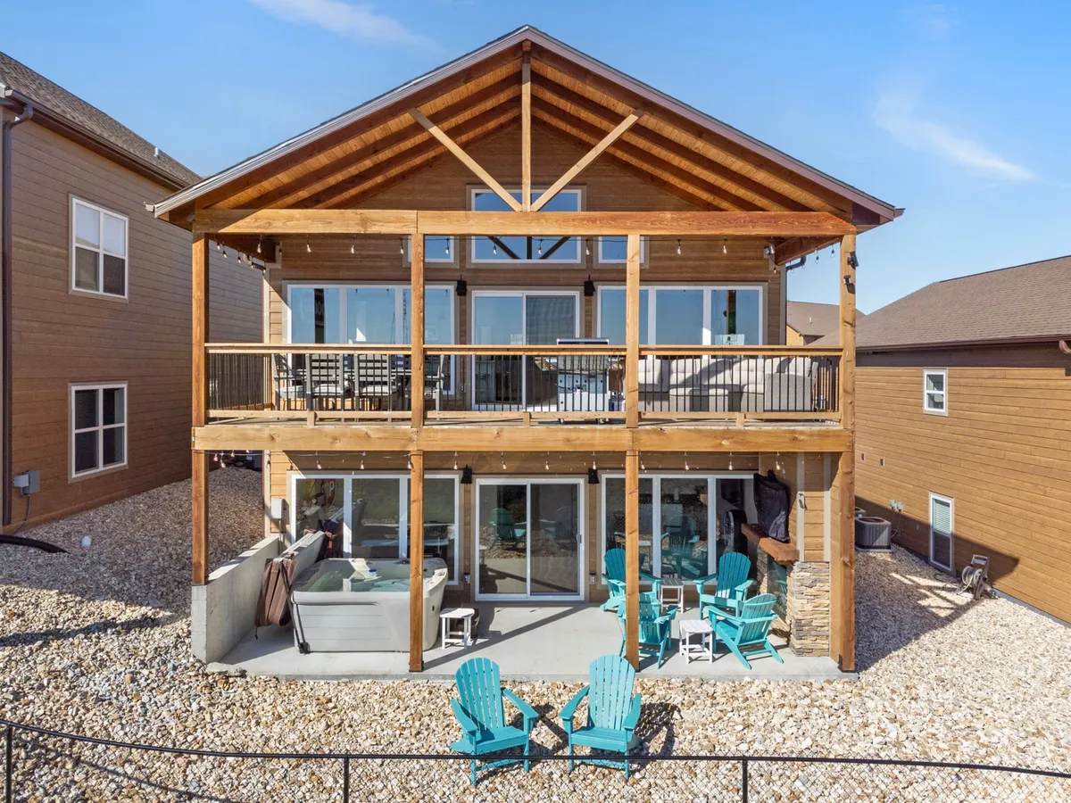A large wooden deck furnished with blue chairs, set against a backdrop of natural greenery. Glass sliding doors lead inside, and the exposed beams give a welcoming feel. The deck looks out onto the wilderness, ideal for relaxing after a day outdoors.