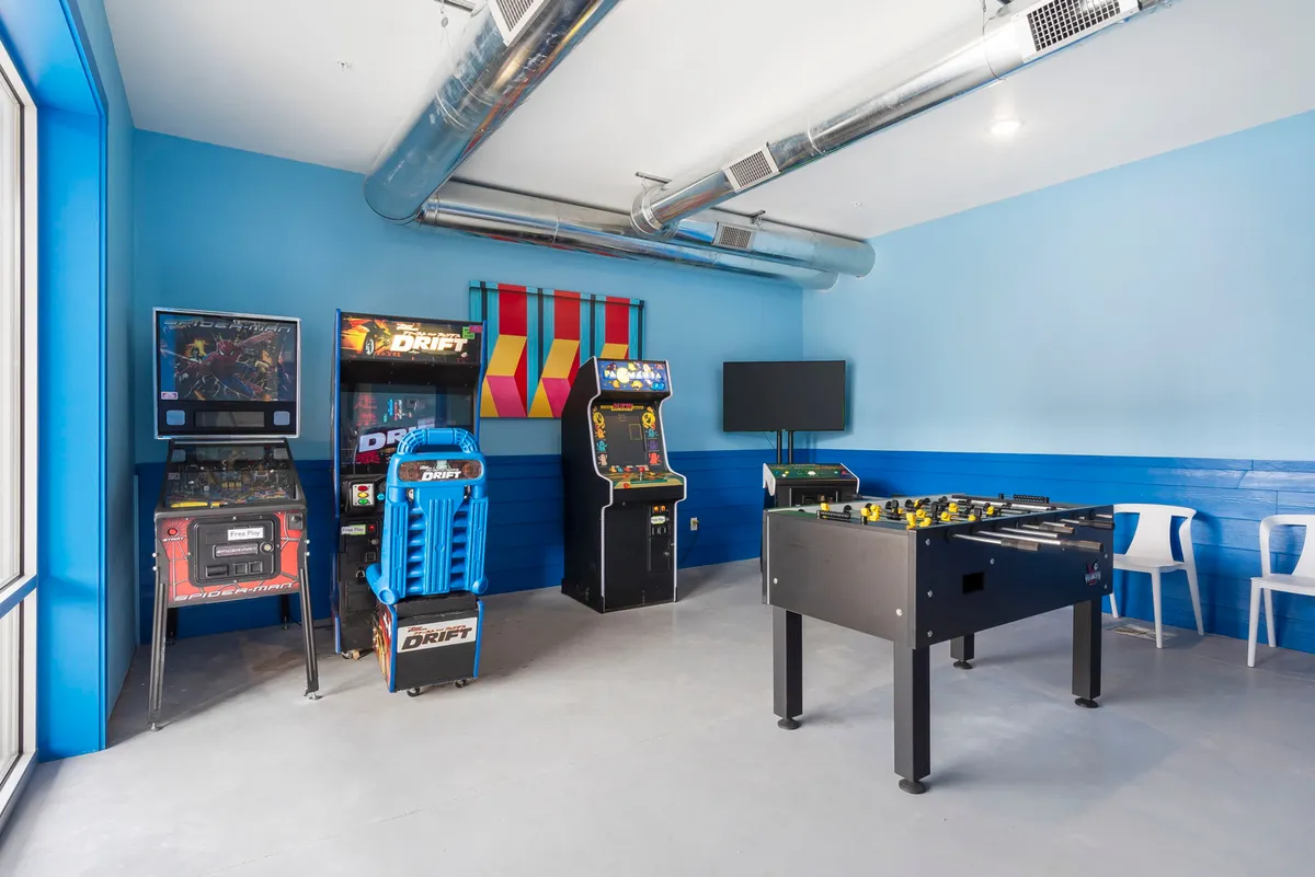 A lively interior shot with multiple arcade machines, a foosball table, and colorful wall decor. The arrangement suggests a space designed for group fun and makes it clear that this is a hub of gaming and socializing.