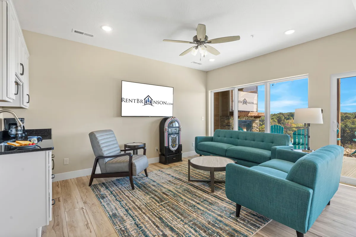 A cozy lounge space featuring a teal sofa and a retro jukebox, with a modern coffee table and large windows letting in natural light. The room feels casual and inviting, perfect for gathering, playing games, or relaxing.