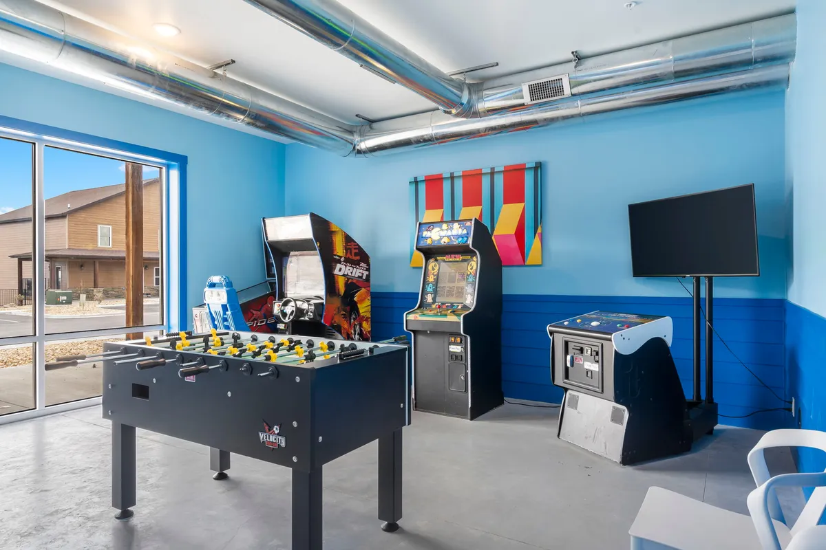 This vibrant interior image centers on a well-equipped game room featuring a foosball table, arcade machines, and a television screen. The space is designed for lively entertainment, with ample room for group activities and friendly competition.